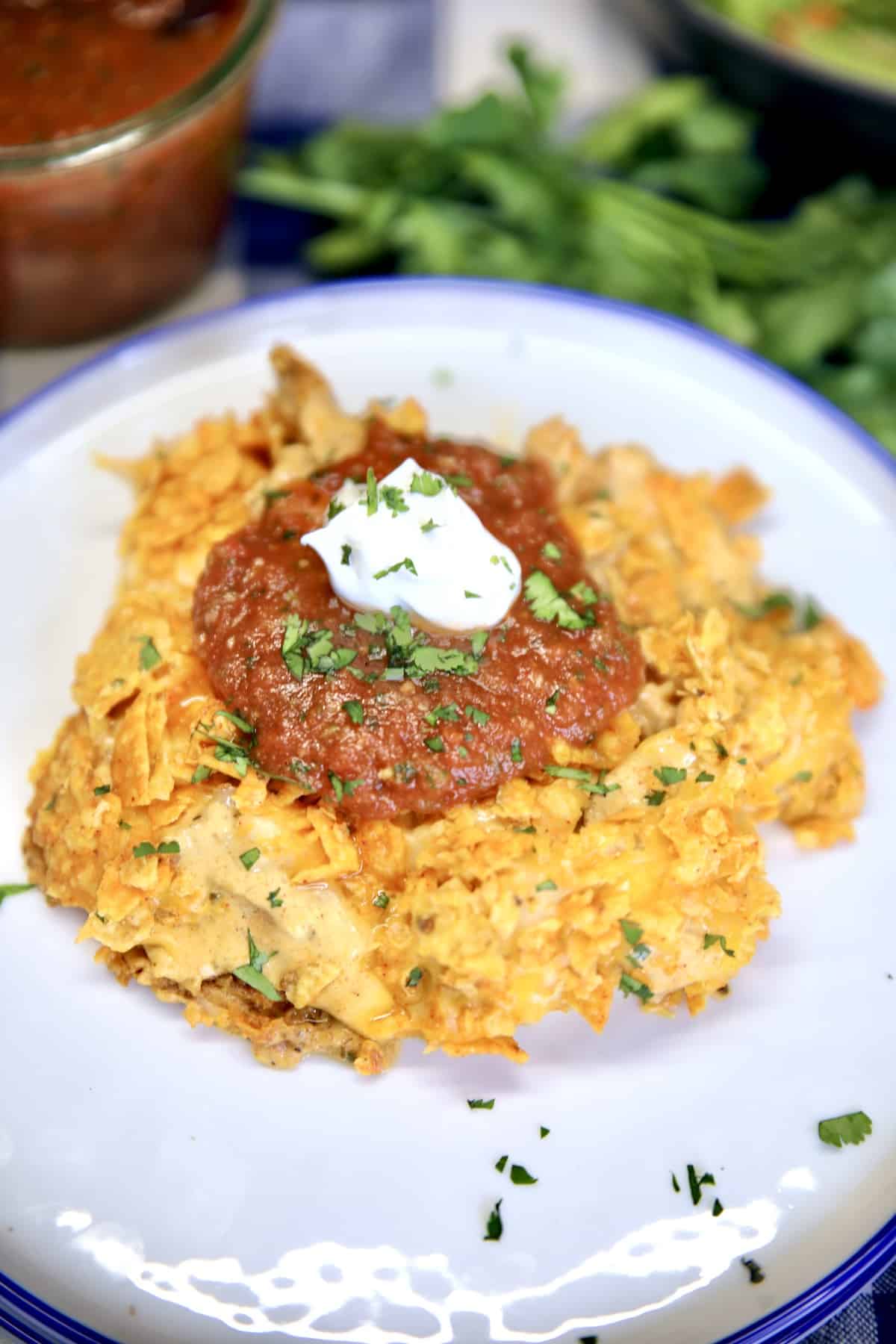 Doritos Chicken Casserole is a family favorite dinner made with a Nacho Cheese Doritos crust and cheesy chicken filling topped off with salsa and sour cream. Doritos chicken casserole on a plate with sour cream and salsa.