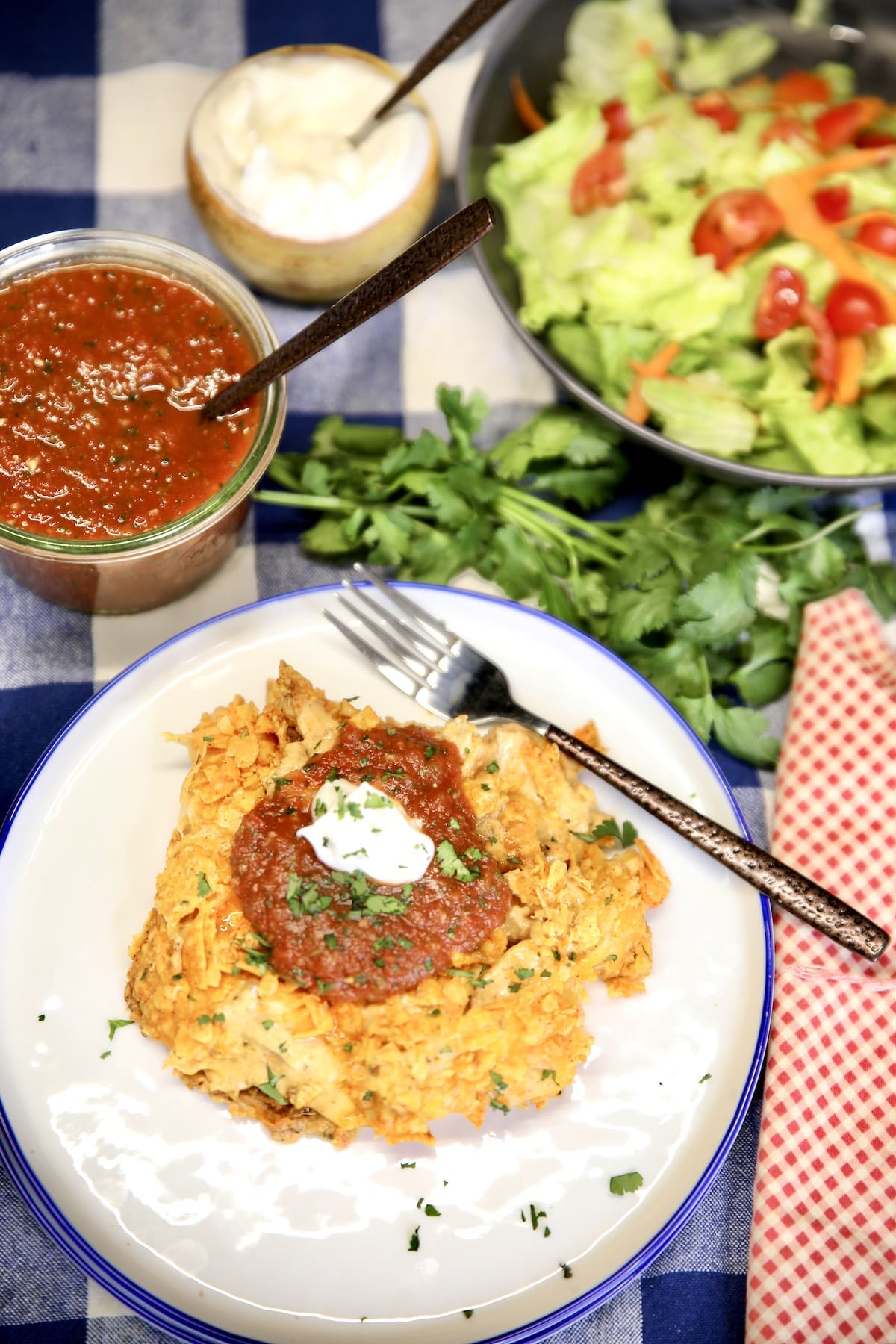 Overhead of doritos chicken casserole with salad, salsa, sour cream.