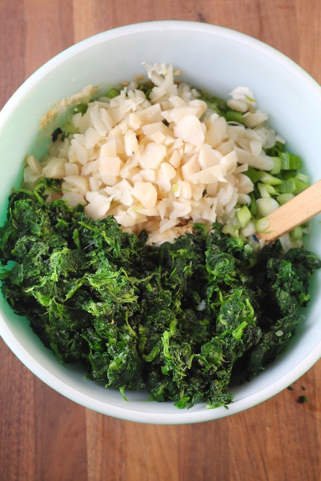 Spinach, water chestnuts and green onions in a bowl with a wood spoon