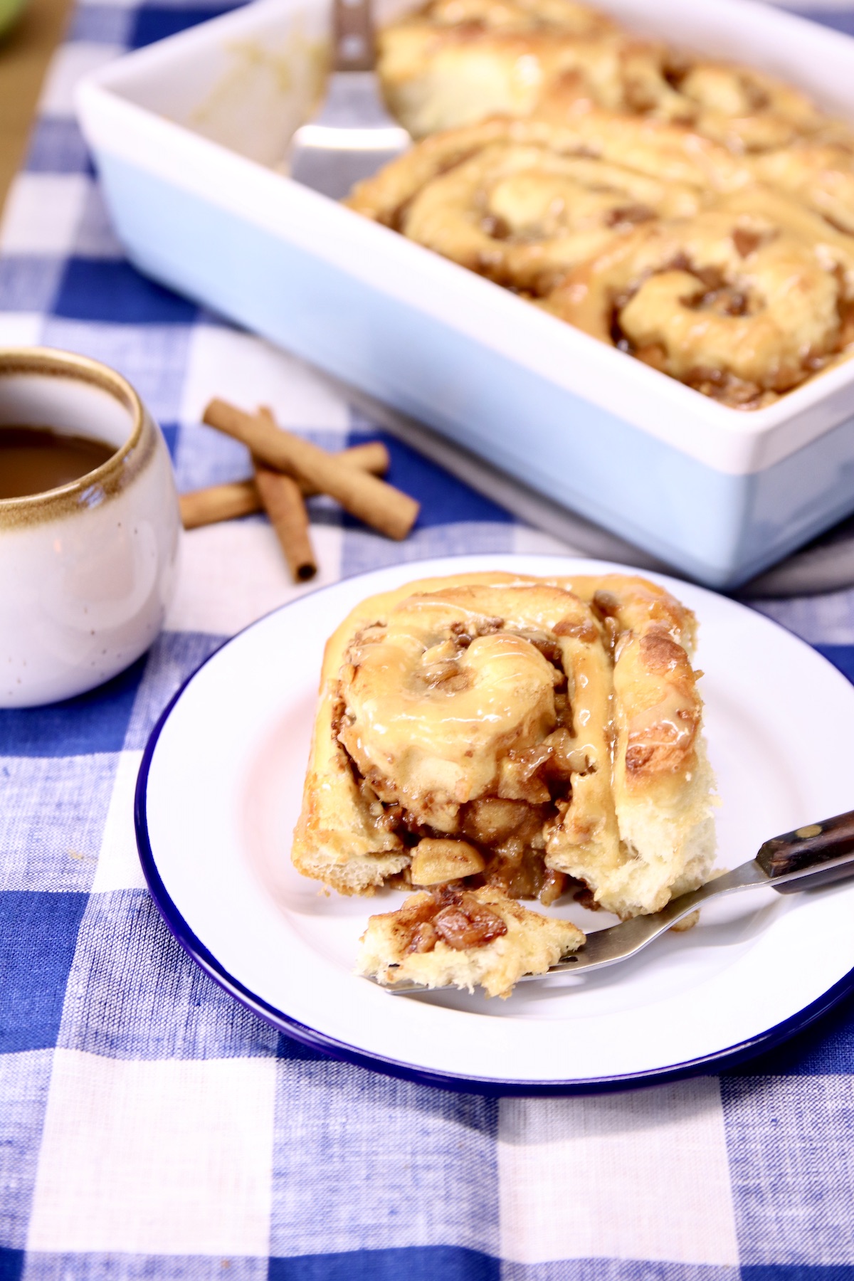 apple cinnamon roll on a plate with piece sliced off on fork - pan in background