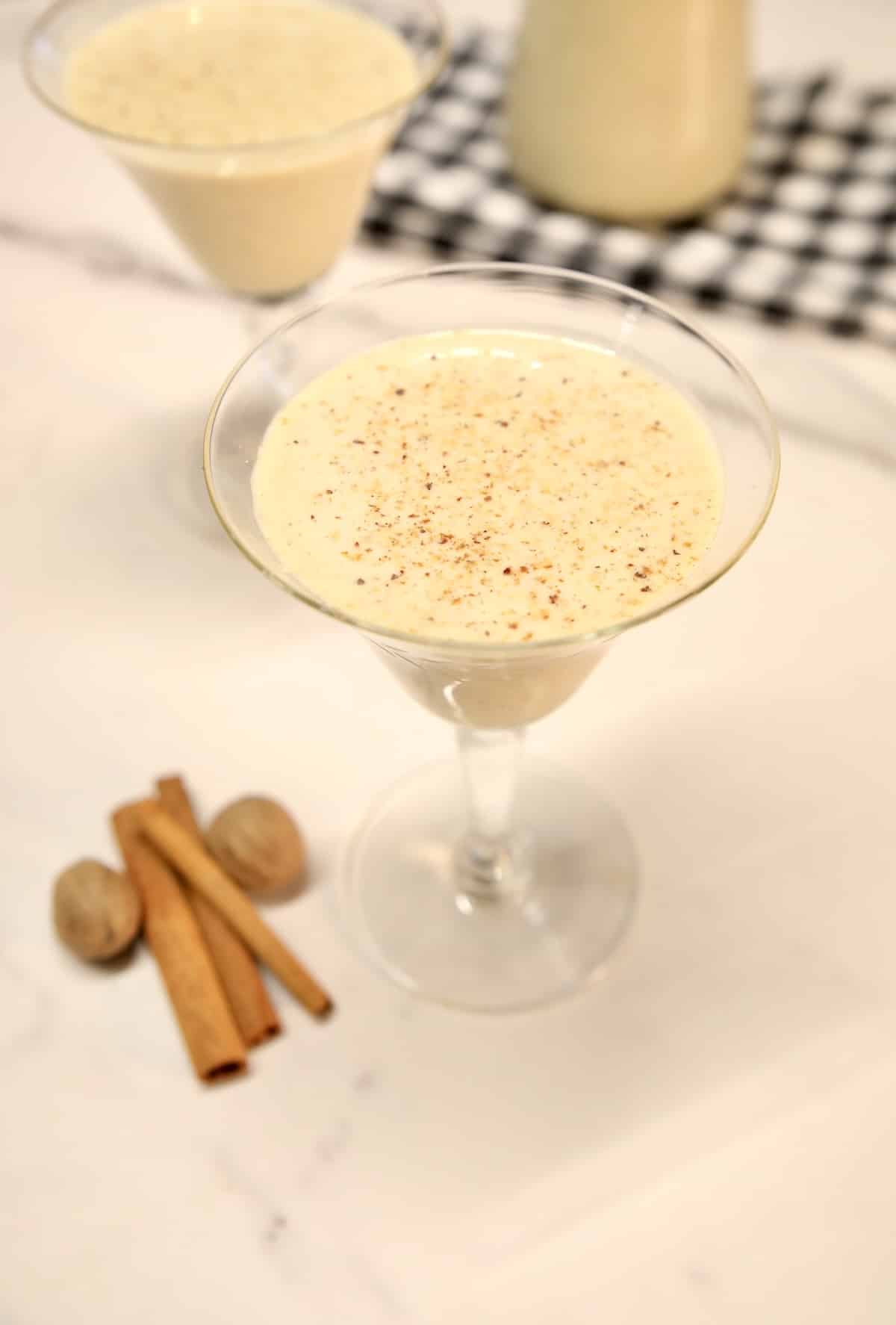Glass of eggnog, cinnamon sticks and whole nutmeg.