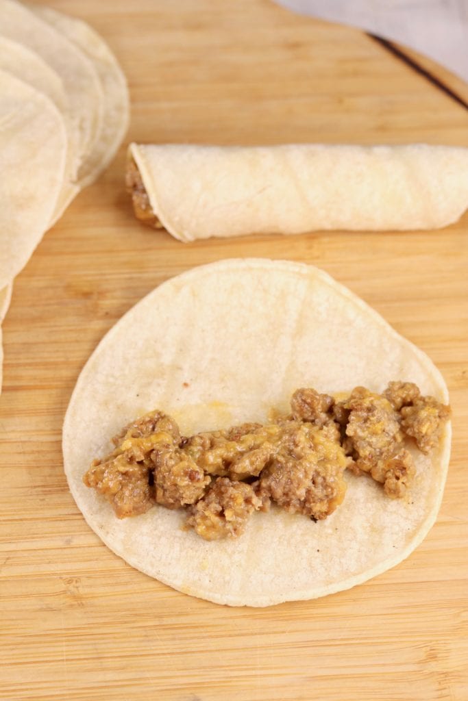 Filling tortillas with cheesy ground beef for taquitos