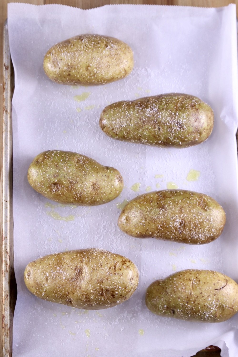 Russet potatoes on a lined baking sheet rubbed with olive oil and salt