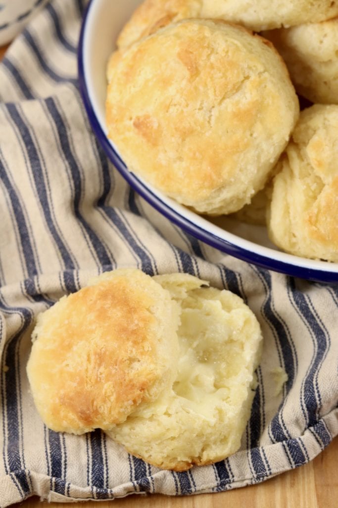 buttered biscuit on a stripe napkin with plate of biscuits
