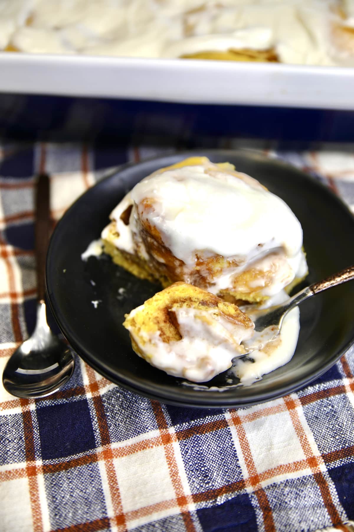 Black dish with pumpkin cinnamon roll and a fork with bite.