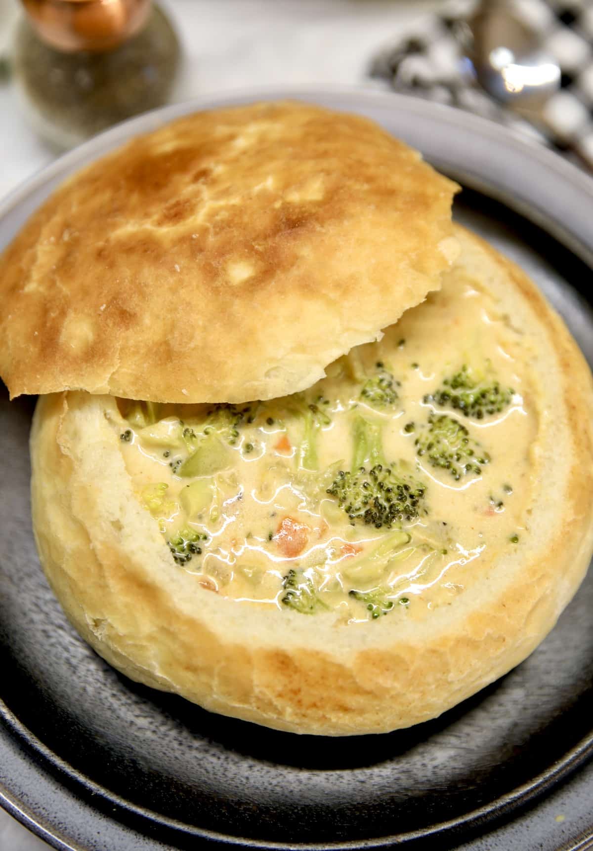 Broccoli cheese soup in a bread bowl on a plate.