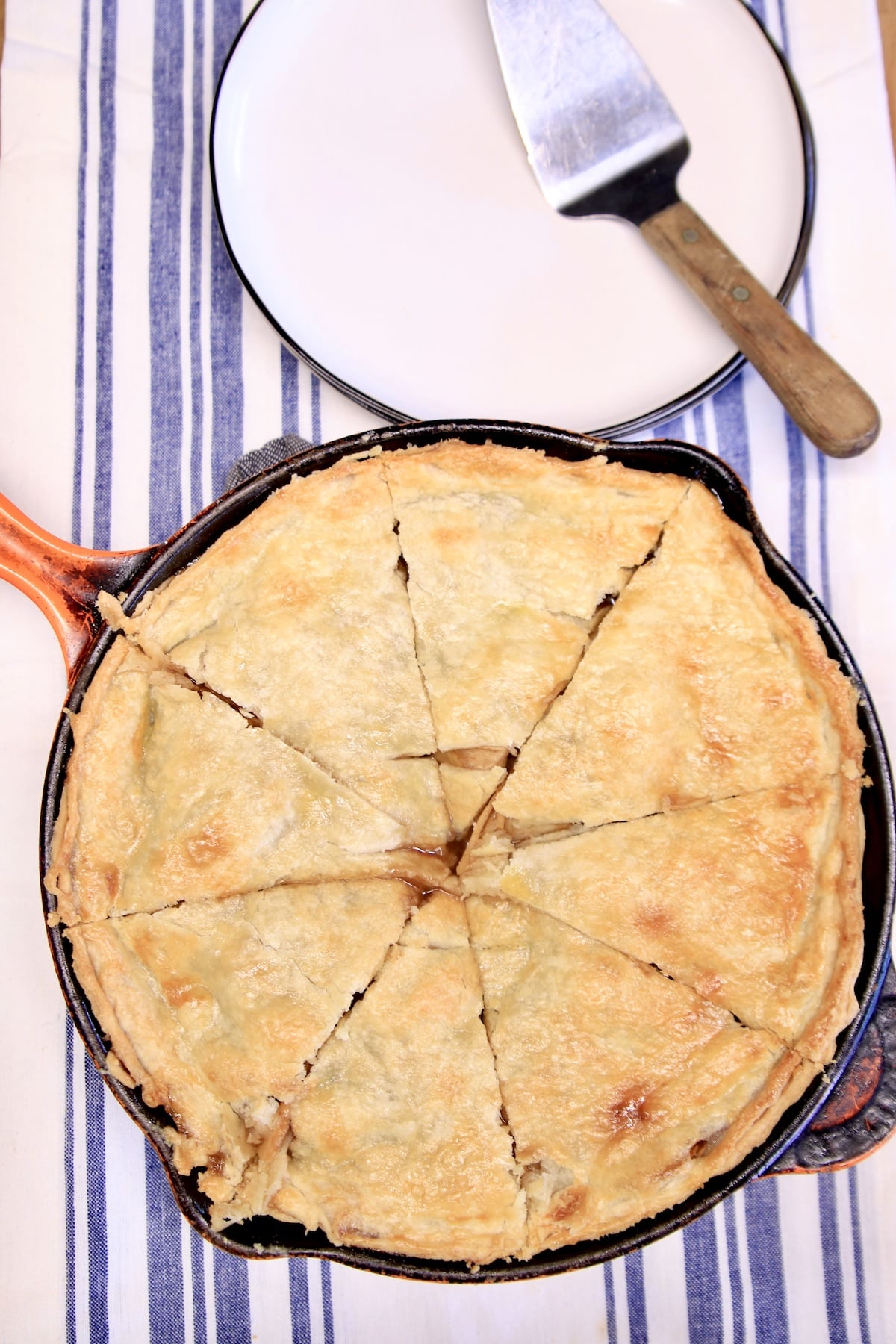 Sliced apple pie in a skillet, dessert plates with pie server.