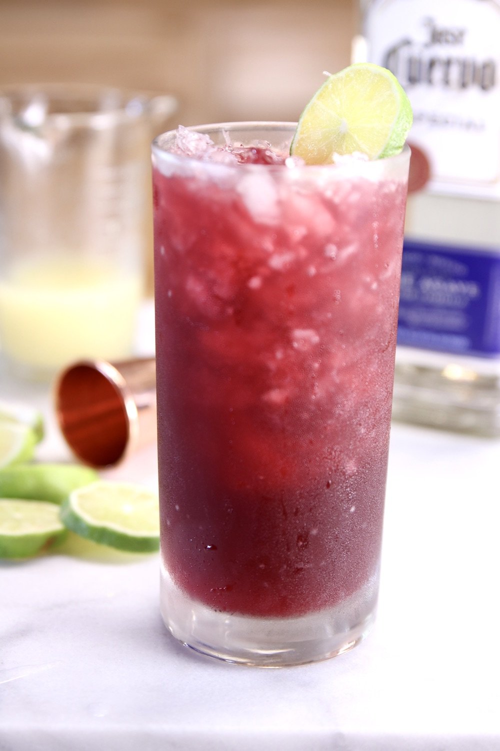 pomegranate margarita with lime garnish, tequila in background