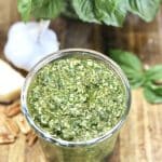 Basil pesto in a jar with garlic bulbs and fresh basil in background.