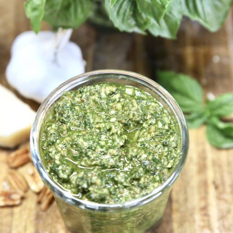 Basil pesto in a jar with garlic bulbs and fresh basil in background.