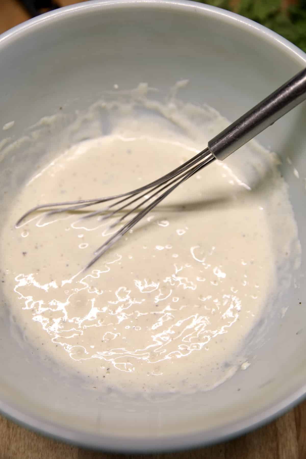 Bowl of pineapple slaw dressing with a whisk.