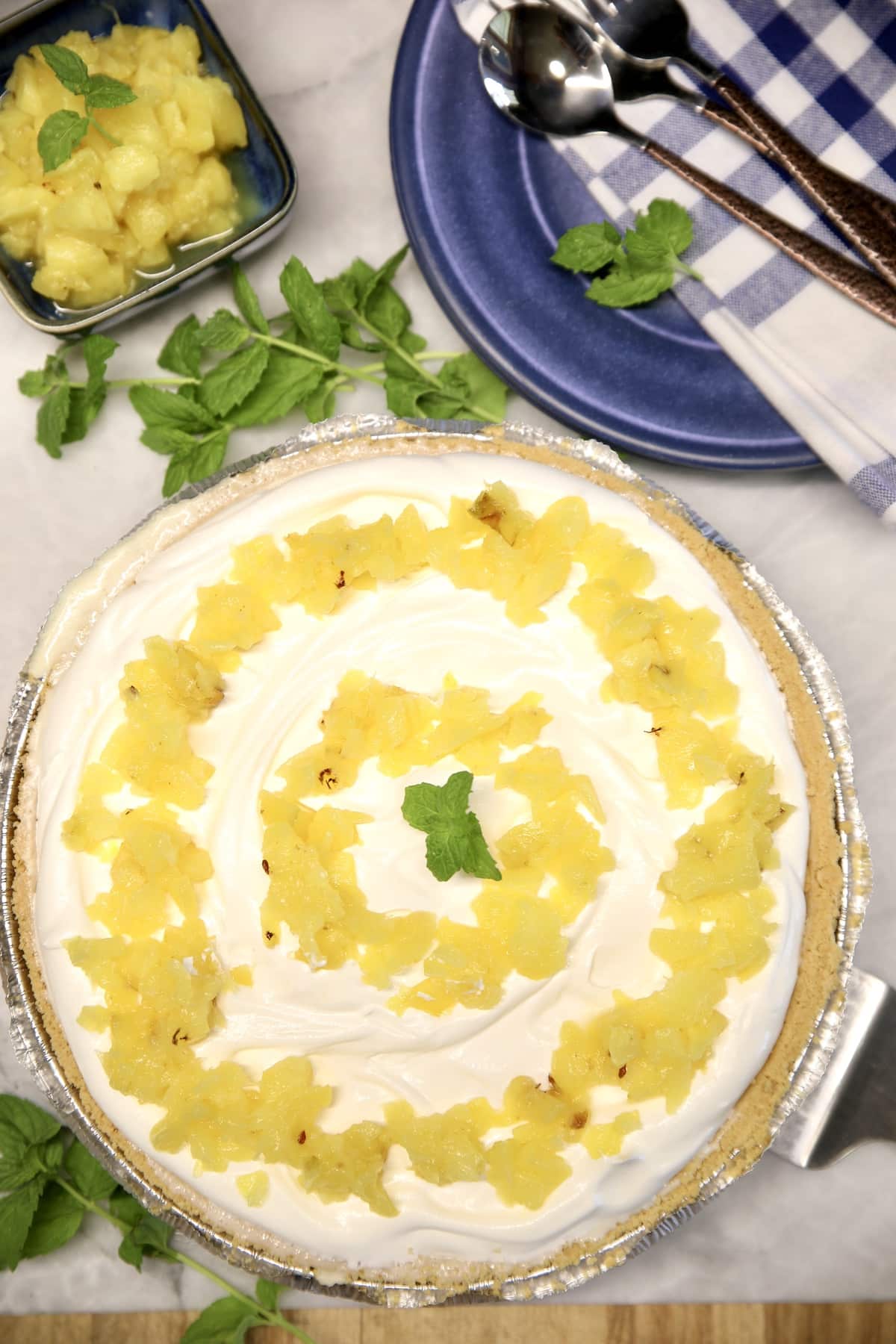 Pineapple pie with bowl of pineapple, plates, napkins, forks.