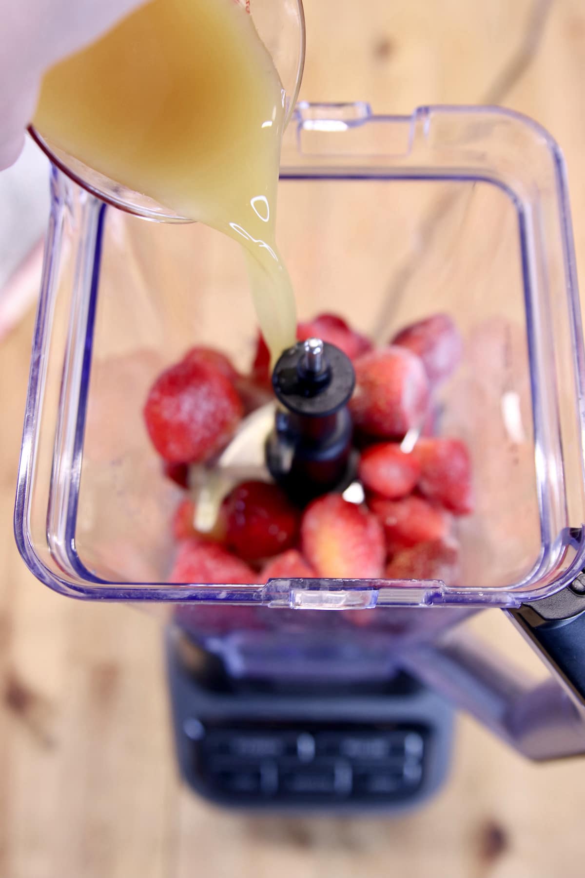 pouring pineapple juice over strawberries in a blender.