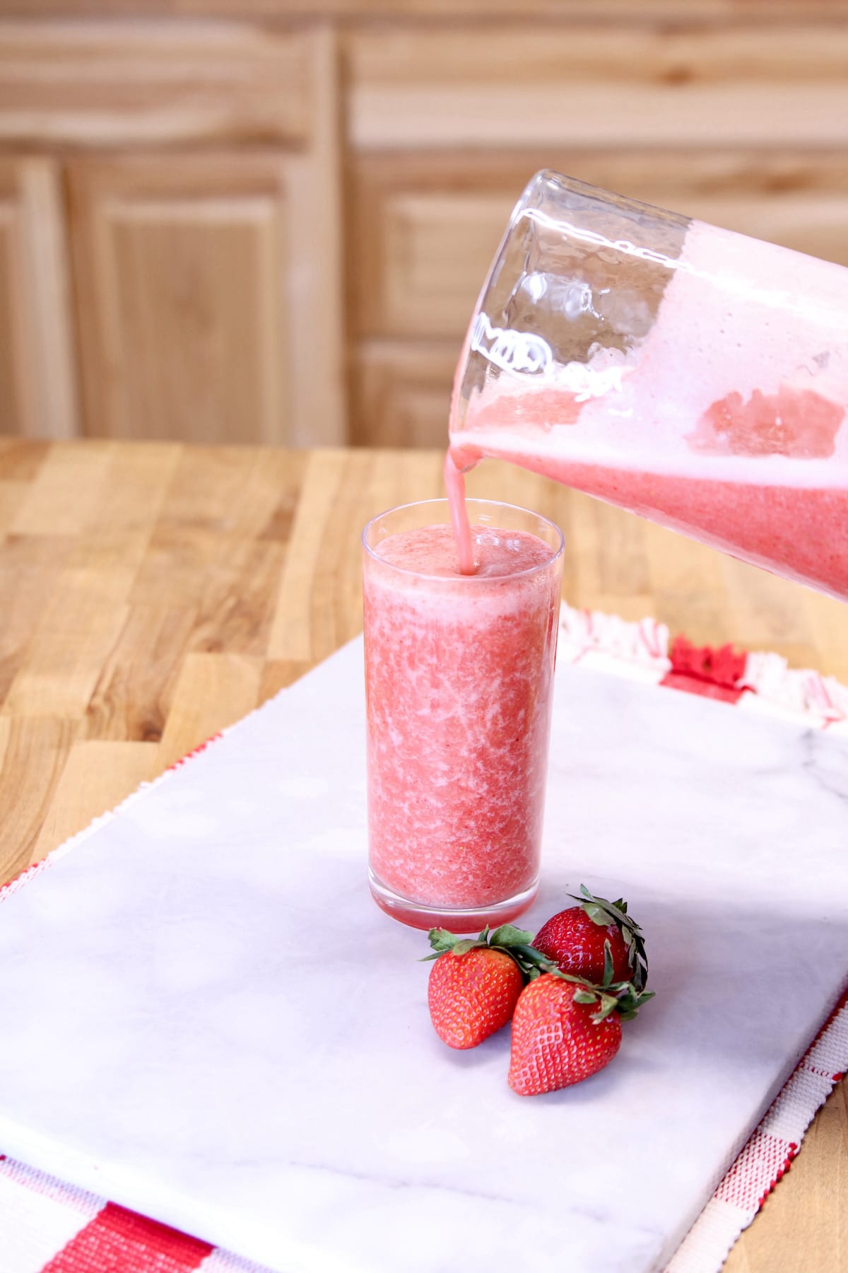 filling collins glass with strawberry cocktail out of a glass pitcher.