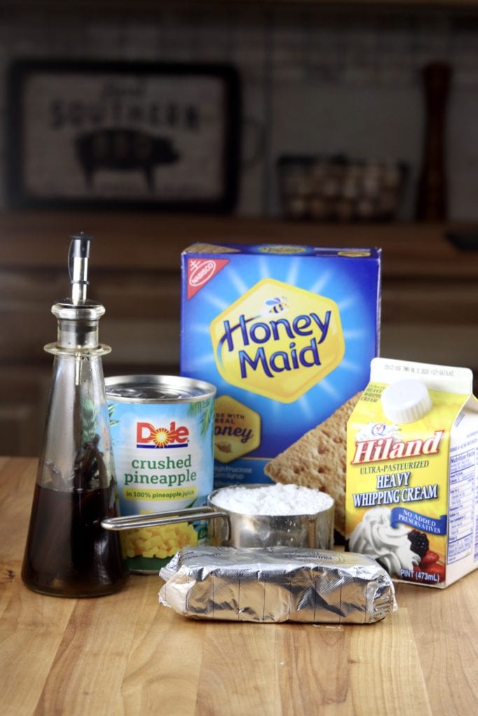 Ingredients for pineapple no bake cheesecake - vanilla extract, cream cheese, crushed pineapple, graham crackers, powdered sugar and heavy cream