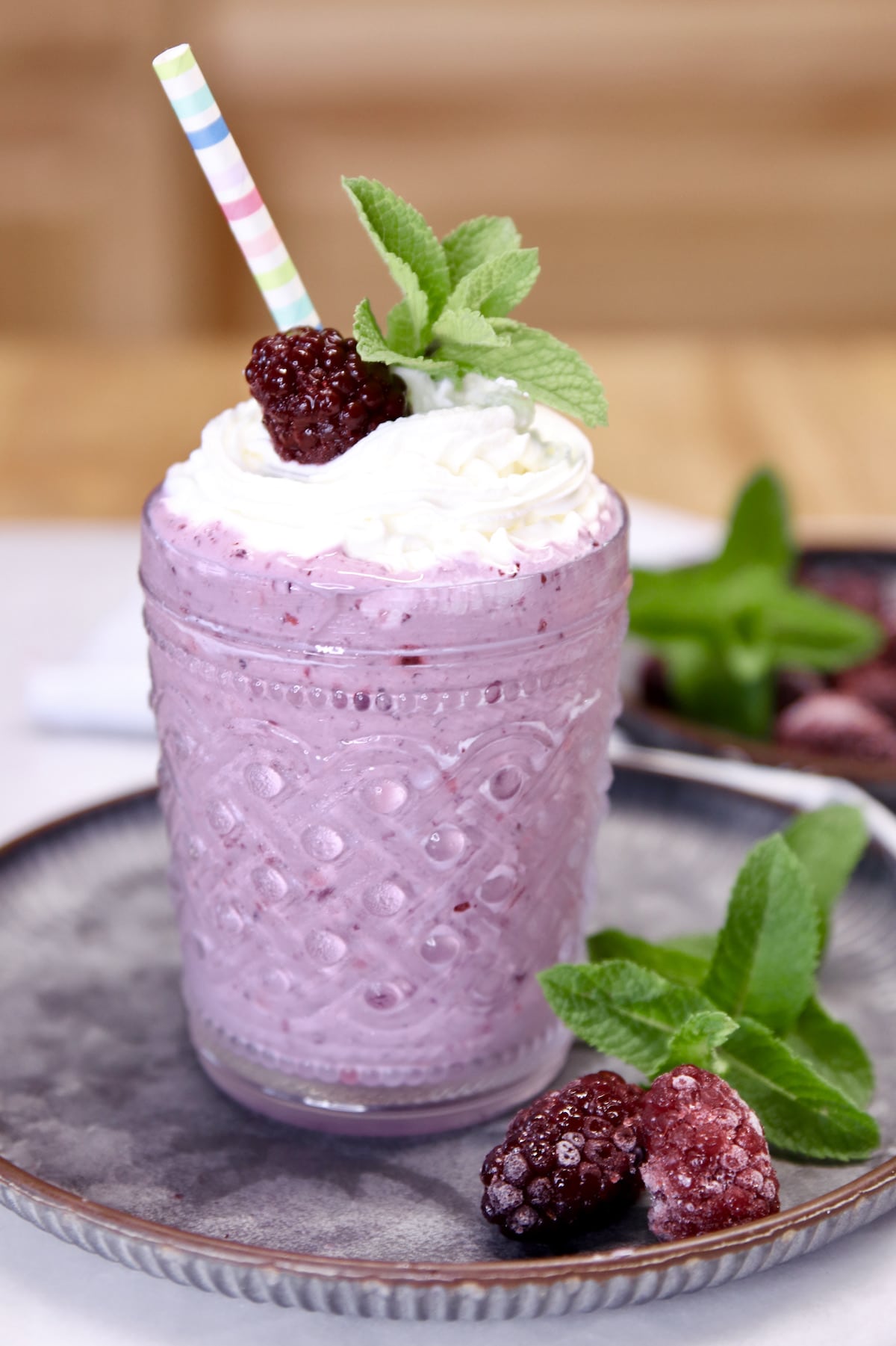 Blackberry milkshake in a glass with striped straw.
