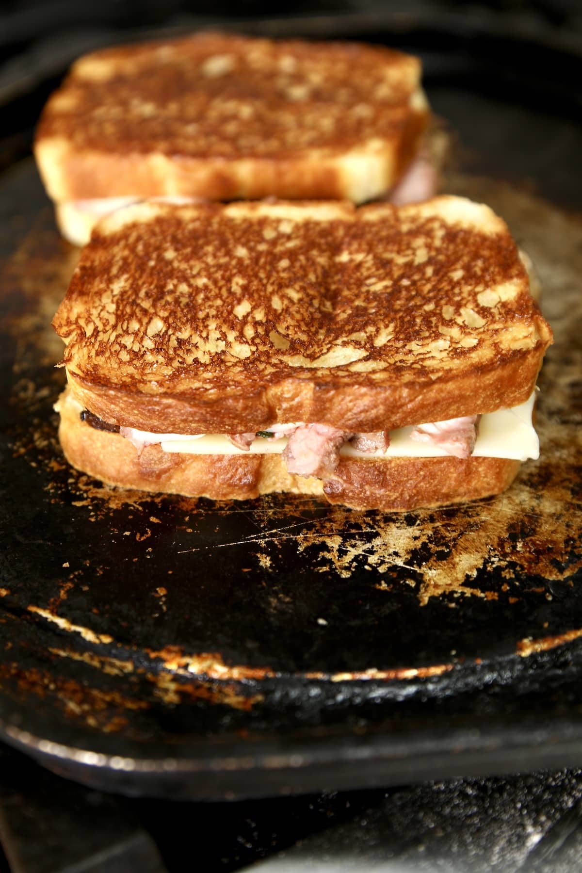 Cooking grilled cheese with steak on a griddle.