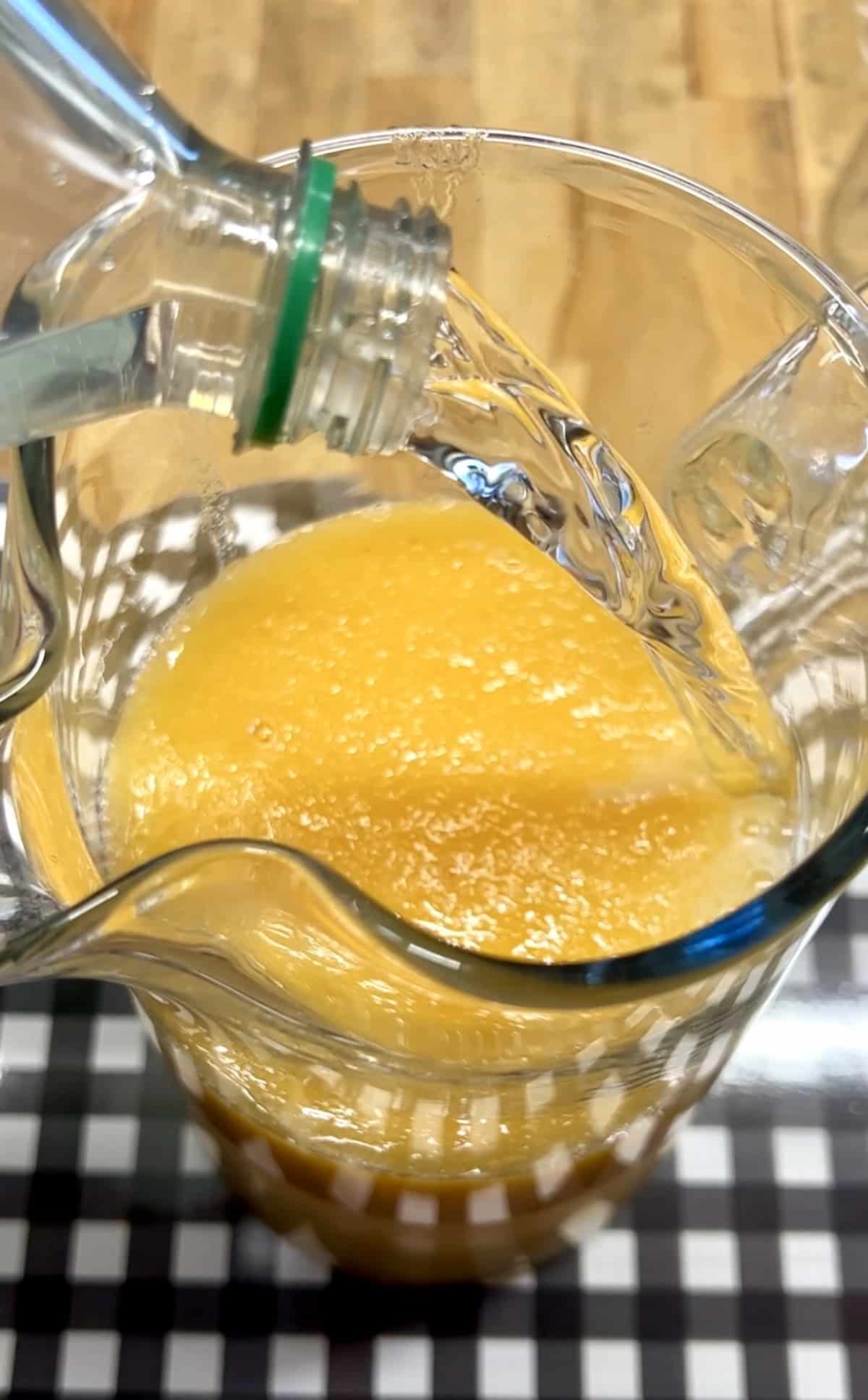 Pouring Sprite into a pitcher with blended peaches. 
