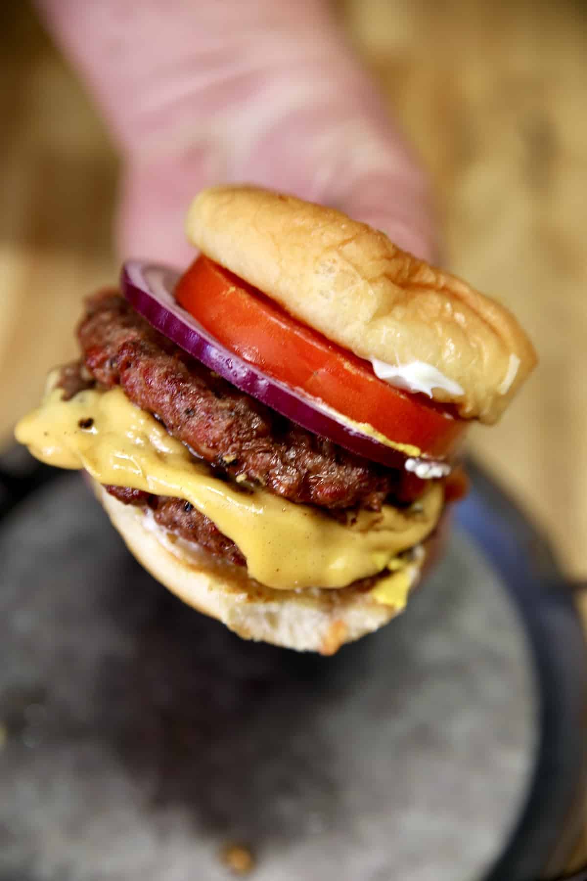 Hand holding double cheeseburger.