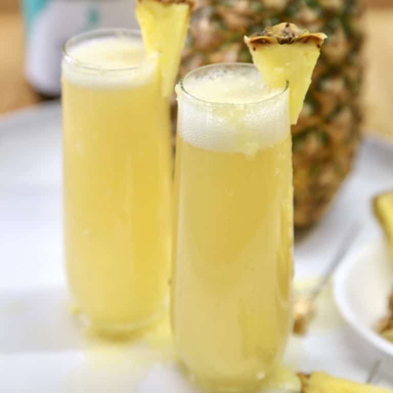 2 champagne glasses with pineapple mimosas.