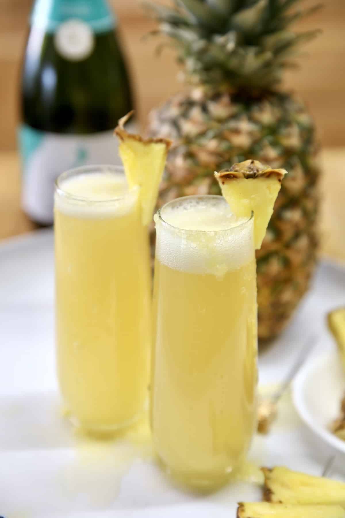 Pineapple Mimosa cocktails for Easter or special occasions. 2 stemless champagne glasses with pineapple mimosas, pineapple garnish.
