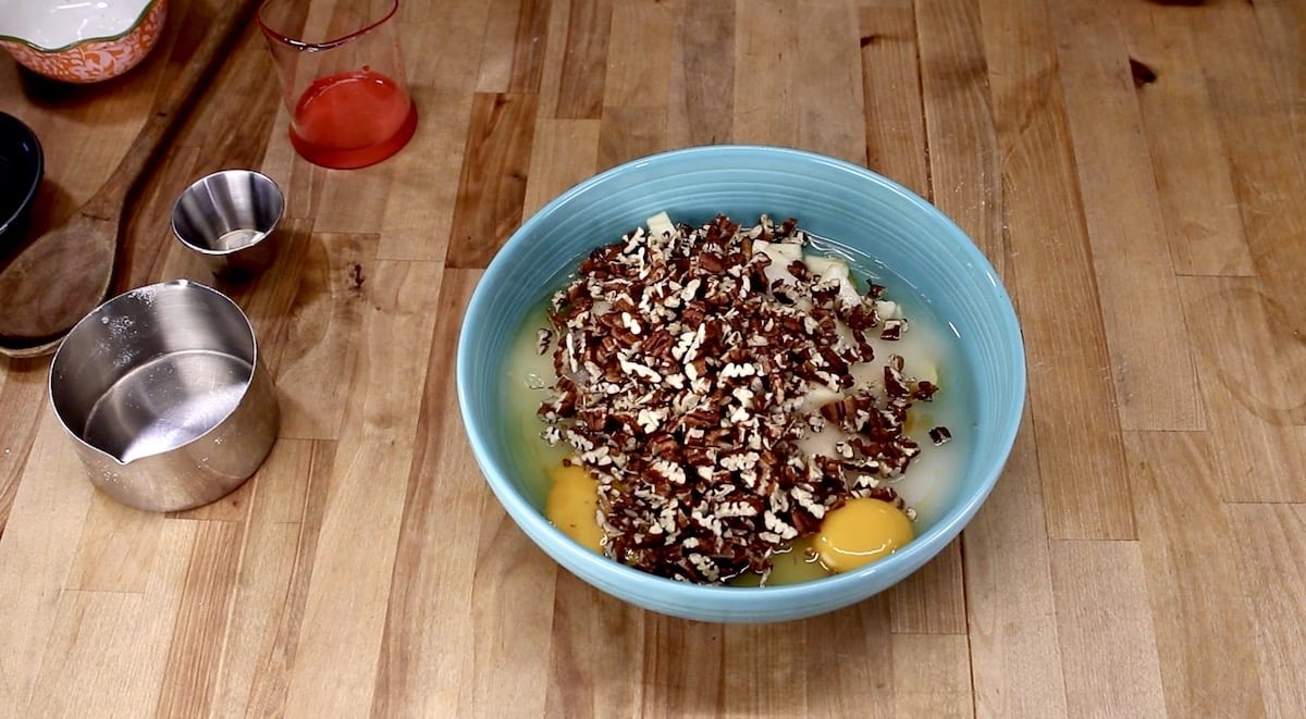 bowl with apple cake ingredients with chopped pecans