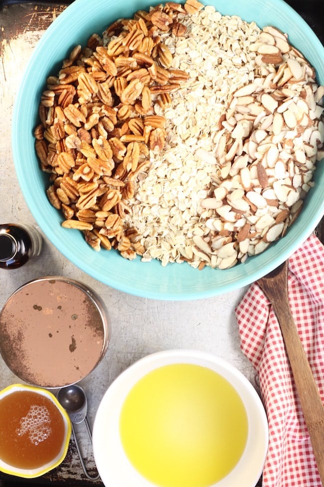Bowl of old fashioned oats, pecans, and sliced almonds, bowl of olive oil, jar of honey and salt cellar with a red check napkin