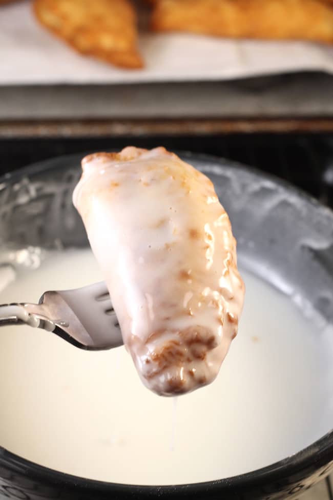 Fried Apple Hand Pie dipped into powdered sugar icing on a fork