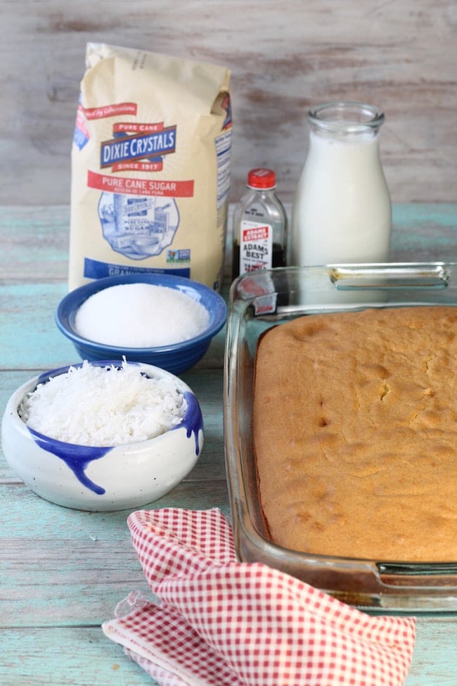 Bag of Sugar, vanilla extract bottle, baked yellow cake, bowl of sugar and bowl of coconut for coconut cream cake recipe