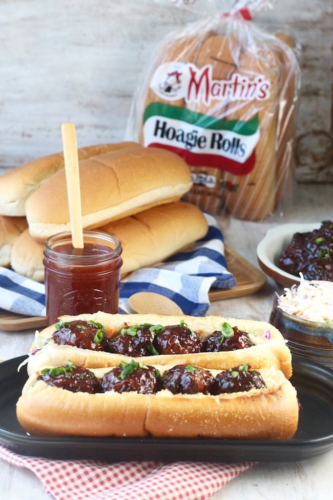 Barbecue Meatball Hoagies with jar of barbecue sauce, hoagie rolls on a platter, package of hoagie buns, dish of meatballs, bowl of coleslaw