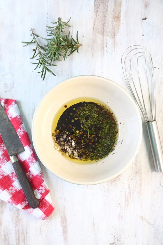 Balsamic marinade with fresh rosemary, a knife on a red check napkin and a whisk on a white background