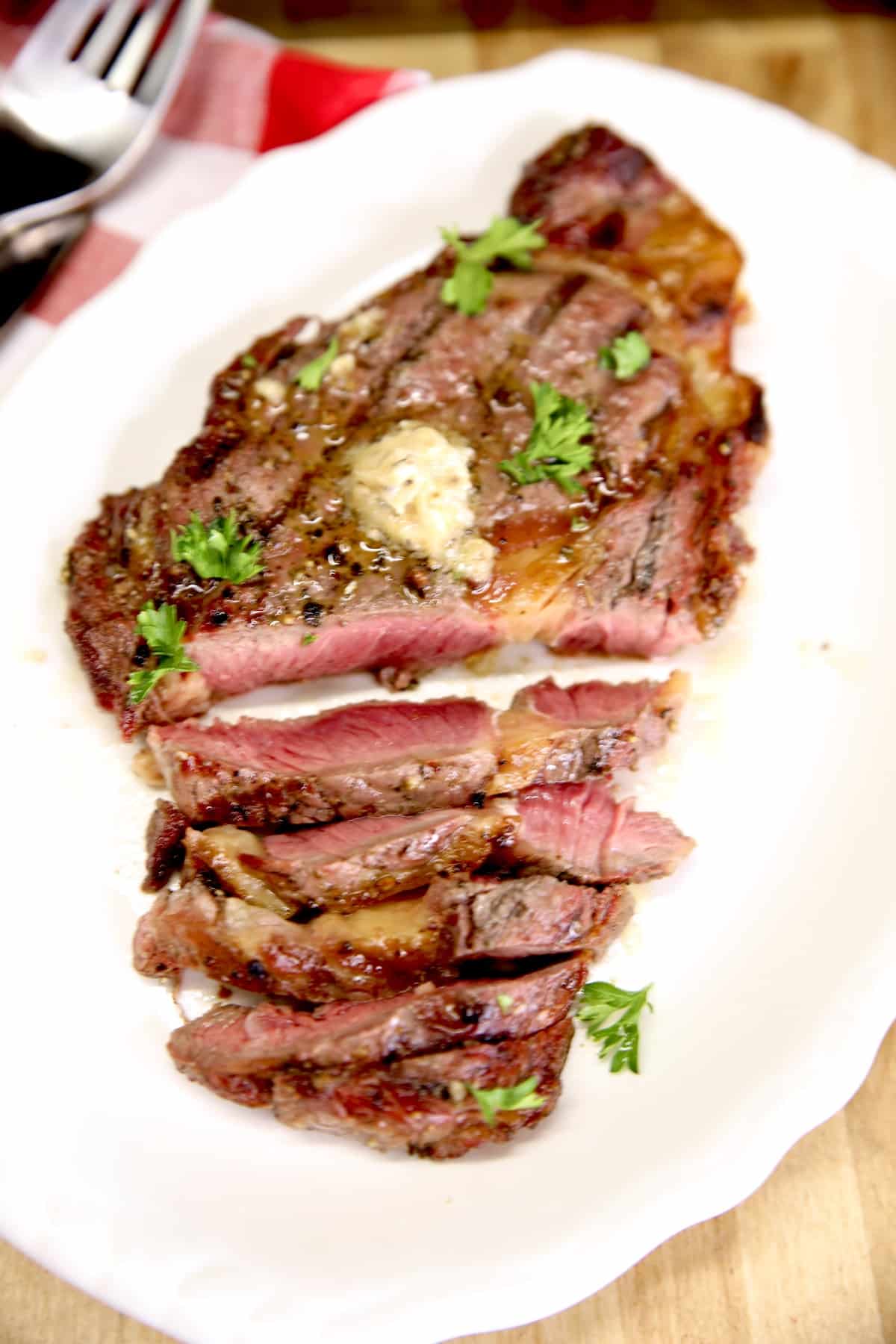 Closeup of steak on a platter, topped with butter, partially sliced.