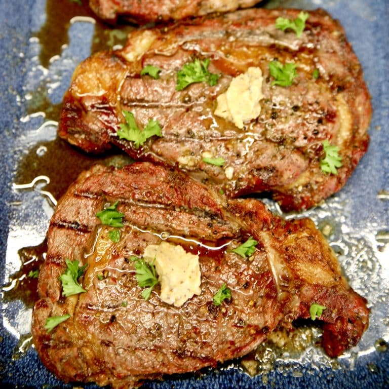 Grilled ribeye steaks with steak butter on a blue platter.