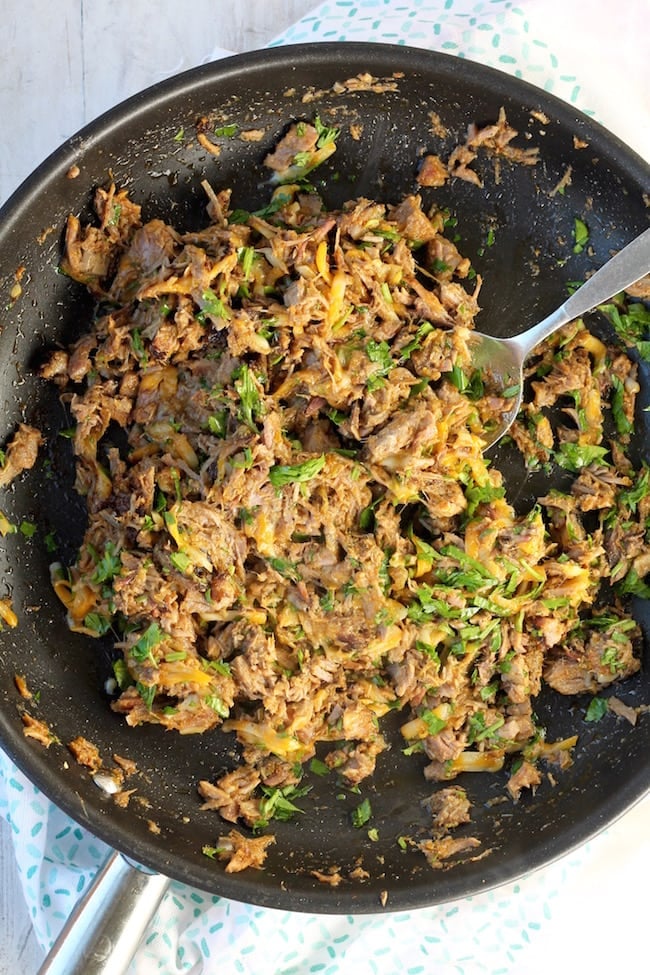 Skillet with shredded brisket, salsa verde and cheese for brisket taquitos