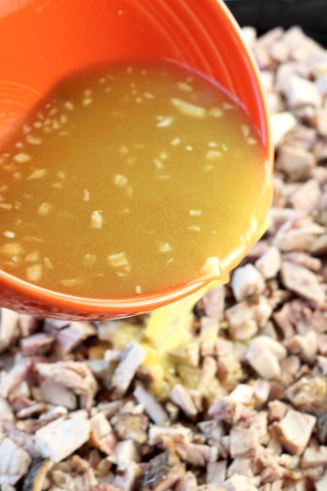 Pouring orange and lime juice mixture over pork for carnitas