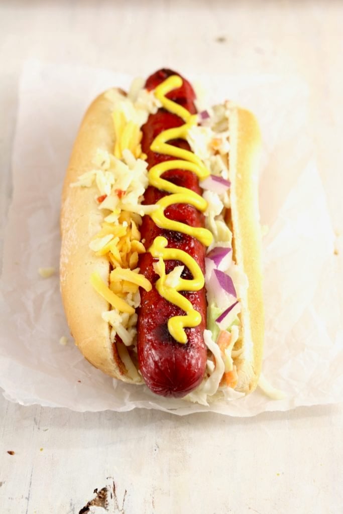 Grilled Hot Dog topped with mustard, slaw, cheese and red onion