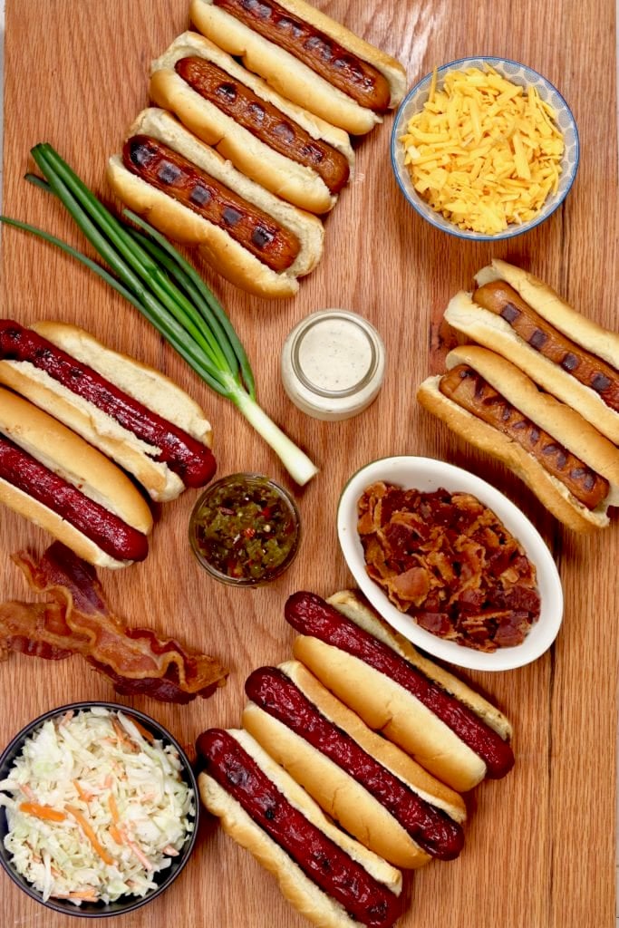 Grilled hot dogs on a board, smoked cheddar, bacon, creamy coleslaw and candied jalapeÃ±os