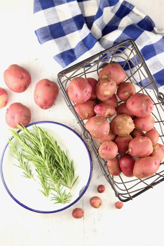 Fresh Rosemary in a white bowl with a wire basket of baby red potatoes