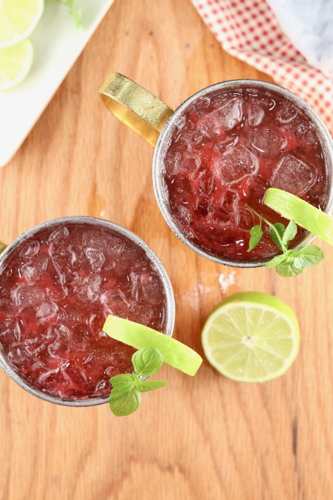 2 Copper Mugs with ice and Moscow Mule cocktails garnished with fresh lime and mint, red and blue napkin in back ground