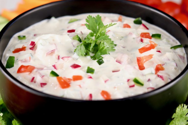 Black bowl of creamy vegetable dip garnished with cliantro