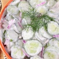 Sliced cucumber salad with creamy dressing and fresh dill in an orange bowl