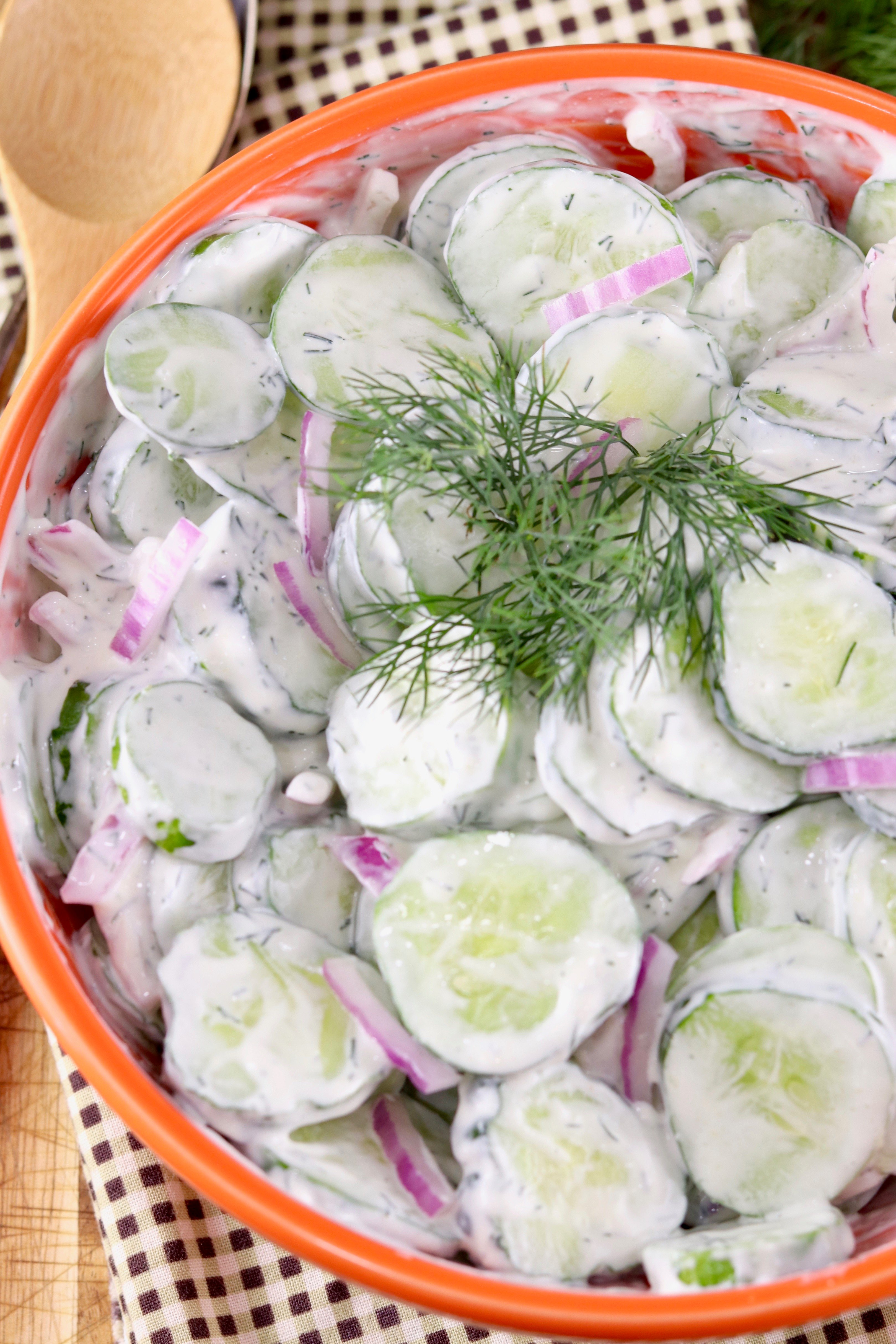 Sliced cucumber salad with creamy dressing and fresh dill in an orange bowl