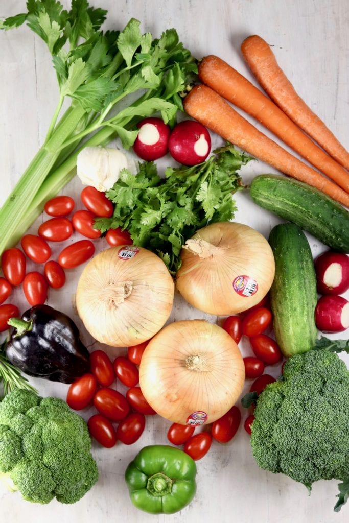 Whole onions, carrots, cucumbers, tomatoes, peppers, cilantro and broccoli on a white board