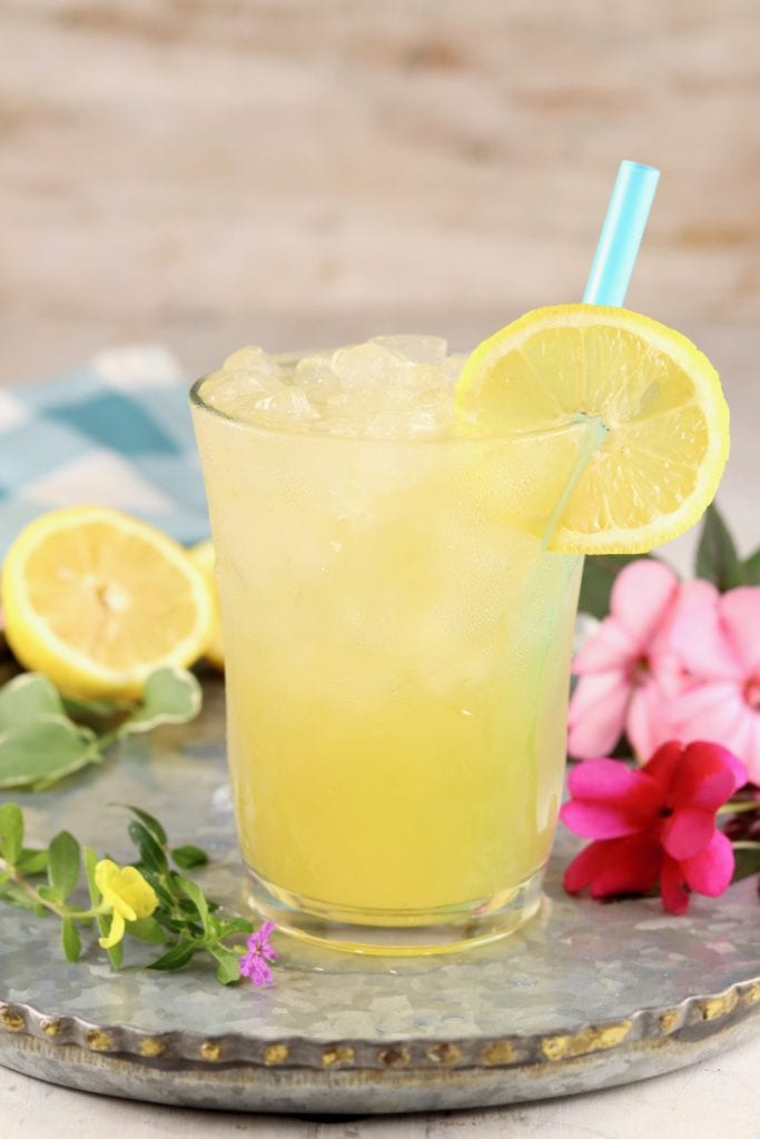 Glass of peach lemonade on a platter with pink flowers and lemon half
