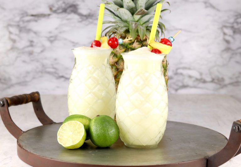 Tray of pineapple glasses with pina colada, fresh line and pineapple in background