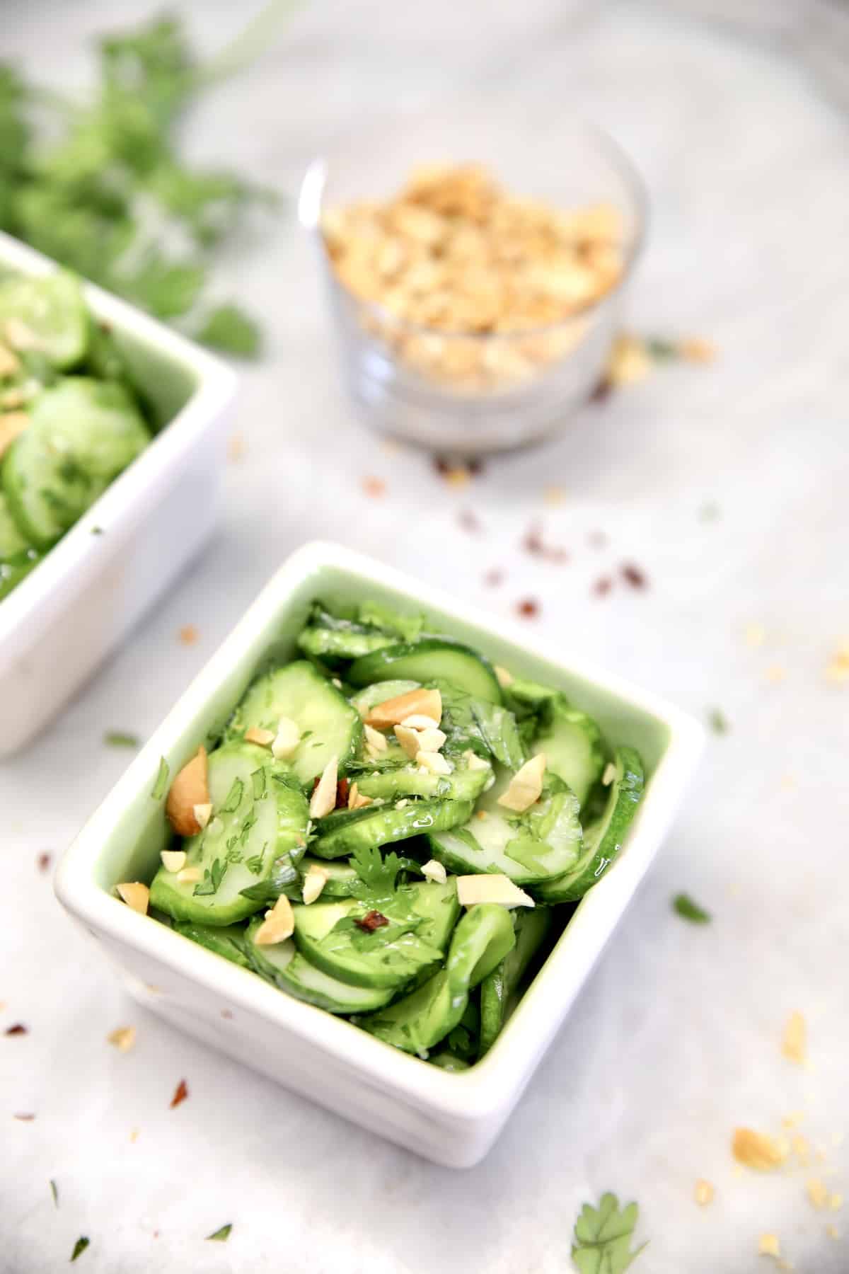 Thai Cucumber salad in a bowl with chopped peanuts in another bowl.