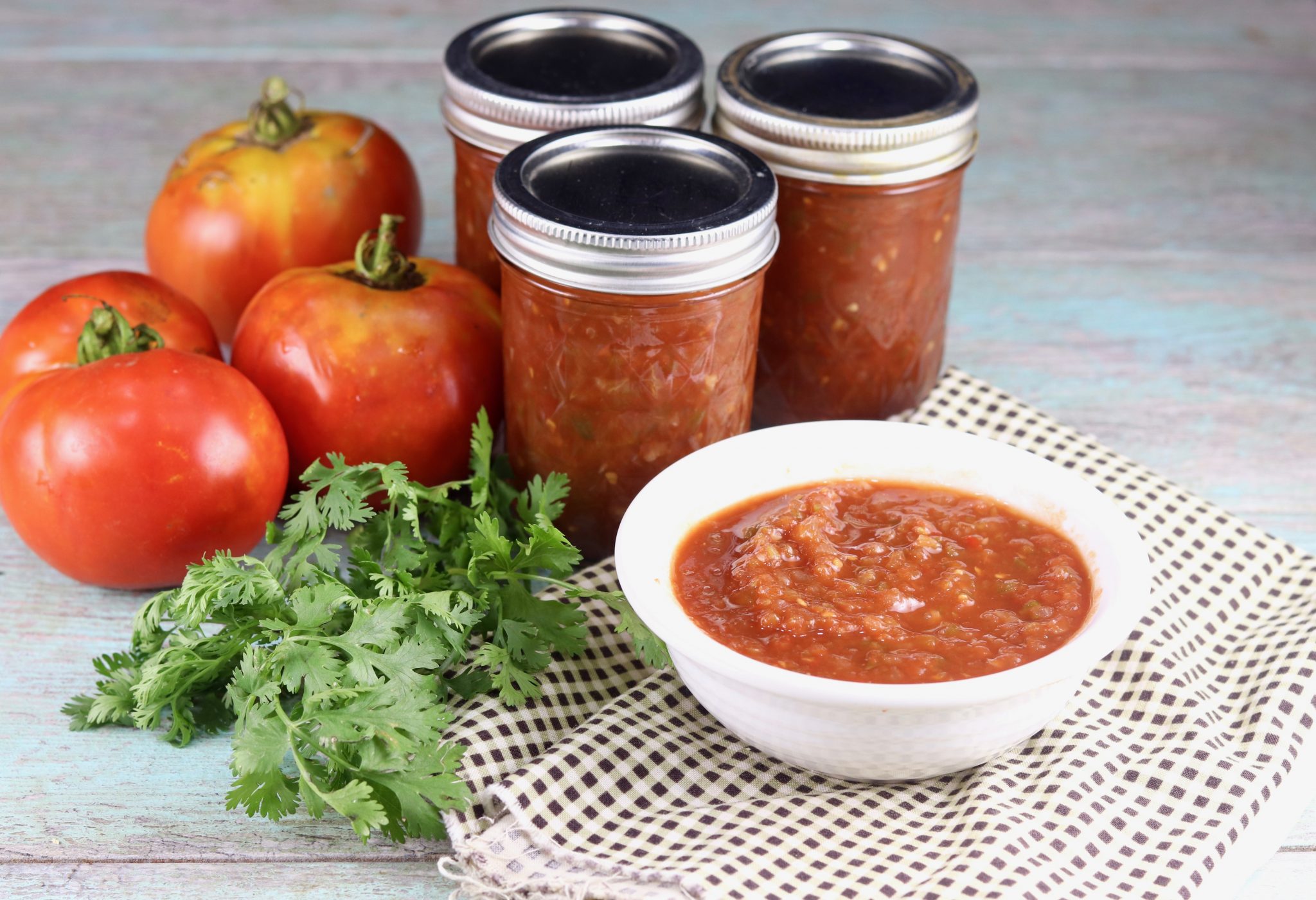 Bowl of salsa with canning jars of homemade salsa, tomatoes and cilantro