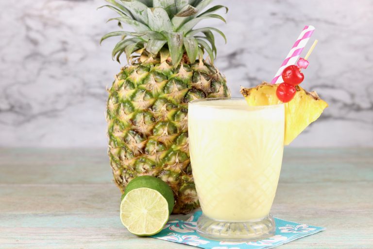 Fresh pineapple and coconut frozen drink with fresh lime and whole pineapple in background