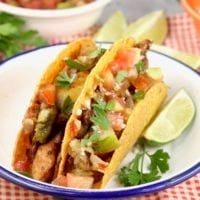 Plate of 2 tacos garnished with cilantro and a lime slice