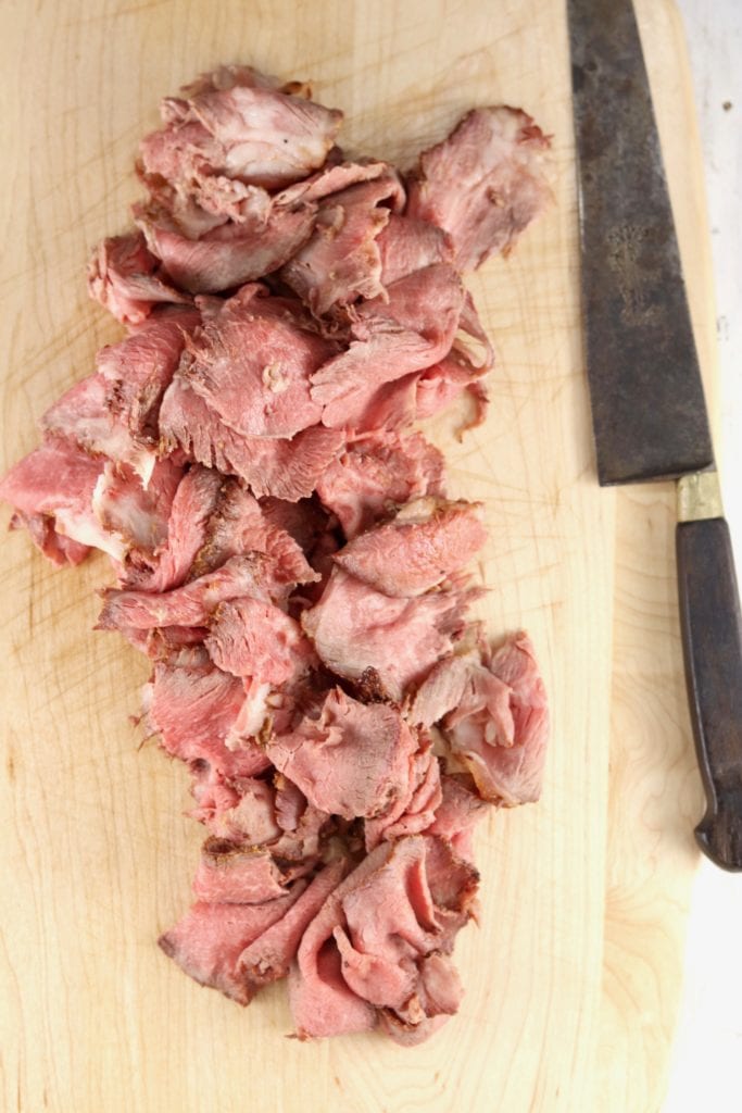 Thin sliced rare roast beef on a cutting board with a knife